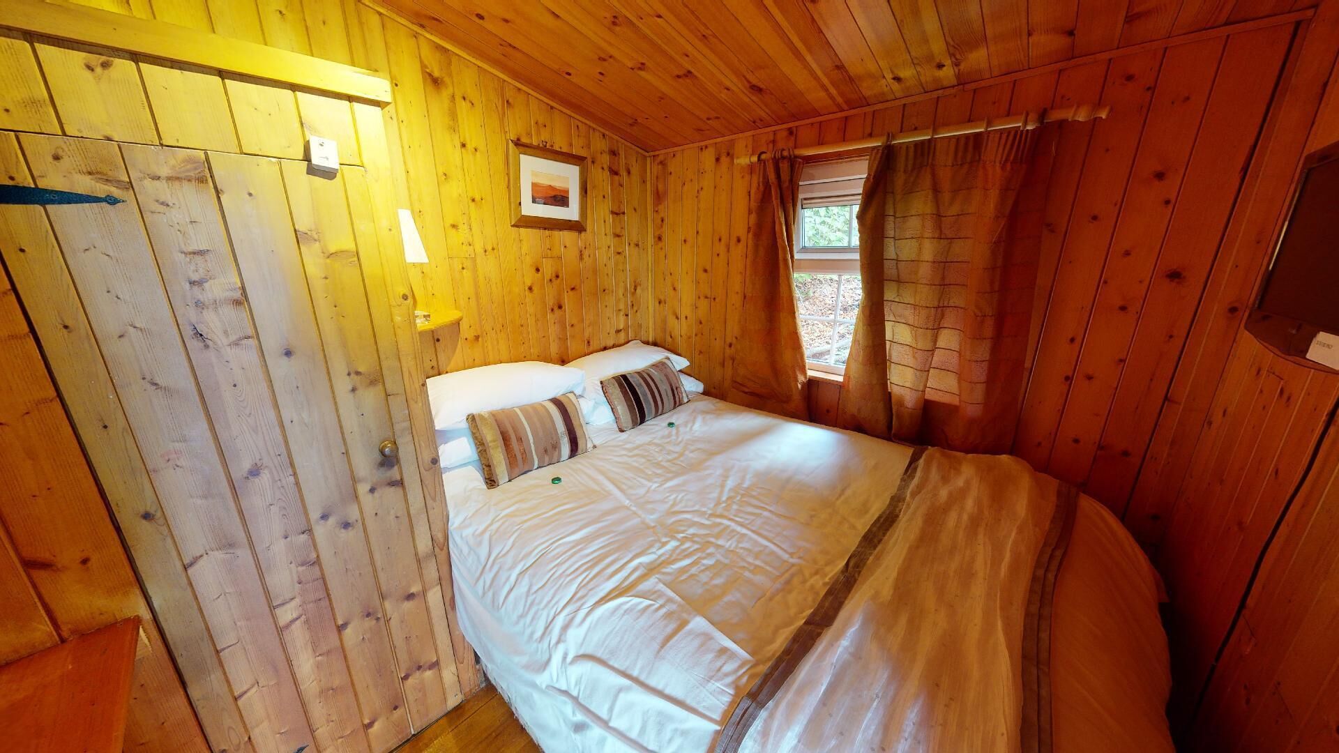 Una habitación de cabaña de madera con una cama, una ventana con cortinas y un cuadro en la pared.