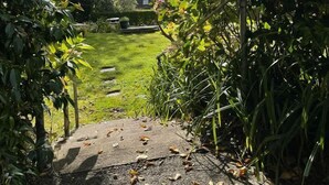 A garden pathway leading to a grassy area with a view of a distant landscape and a building. - Robin Hill House Heritage B&B (Cobh)