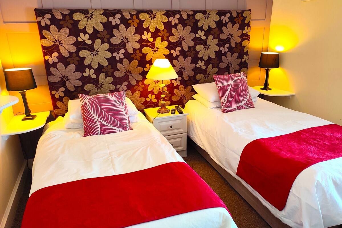 A hotel room with two beds, each with a red and white bedspread, a floral-patterned headboard, and bedside lamps.