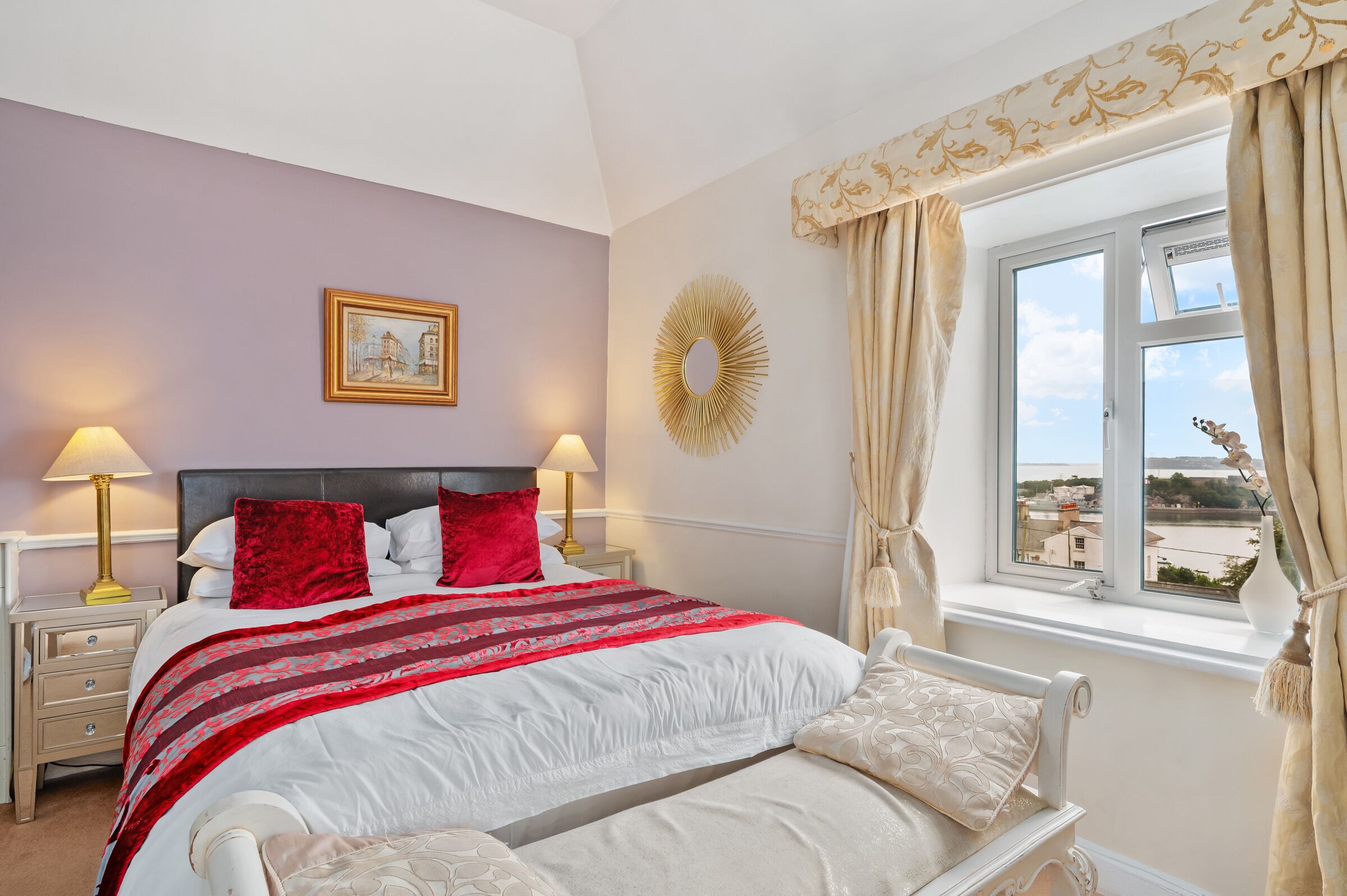 Una camera da letto con un letto, due comodini, un tavolino, una finestra con tende e uno specchio fissato alla parete.