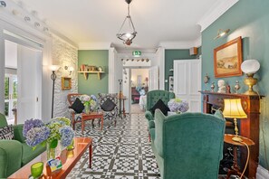 A hotel lobby with a checkered floor, green upholstered chairs, a chandelier, and a fireplace with a lamp. - Robin Hill House Heritage B&B (Cobh)