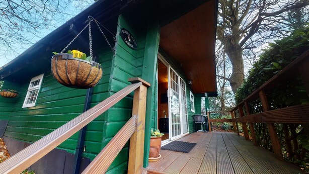 A green wooden lodge with a wooden deck, a hanging basket, and a sign reading "Robin File Lodge". - Robin Hill House Heritage B&B (Cobh)