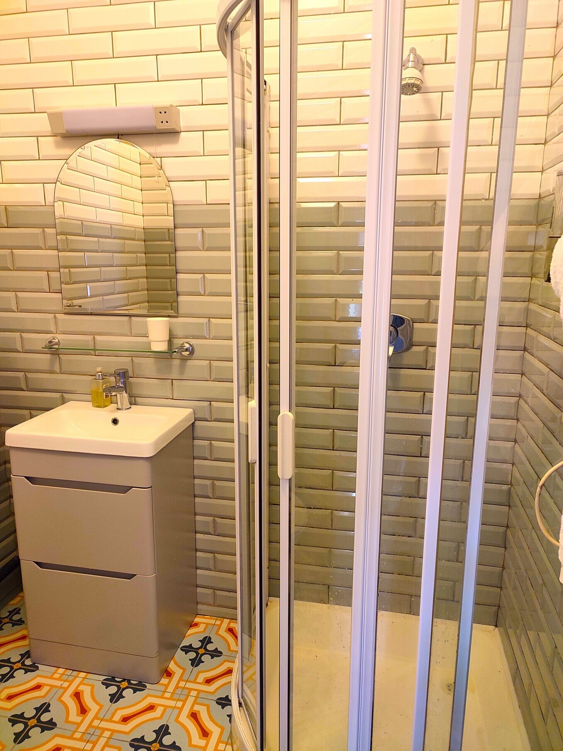 Un baño con cabina de ducha de vidrio, un lavabo con espejo y suelo estampado.