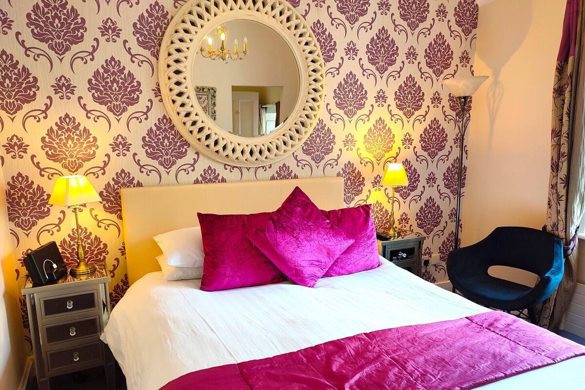 A hotel room with a large bed, two bedside lamps, a mirror, and a chair.