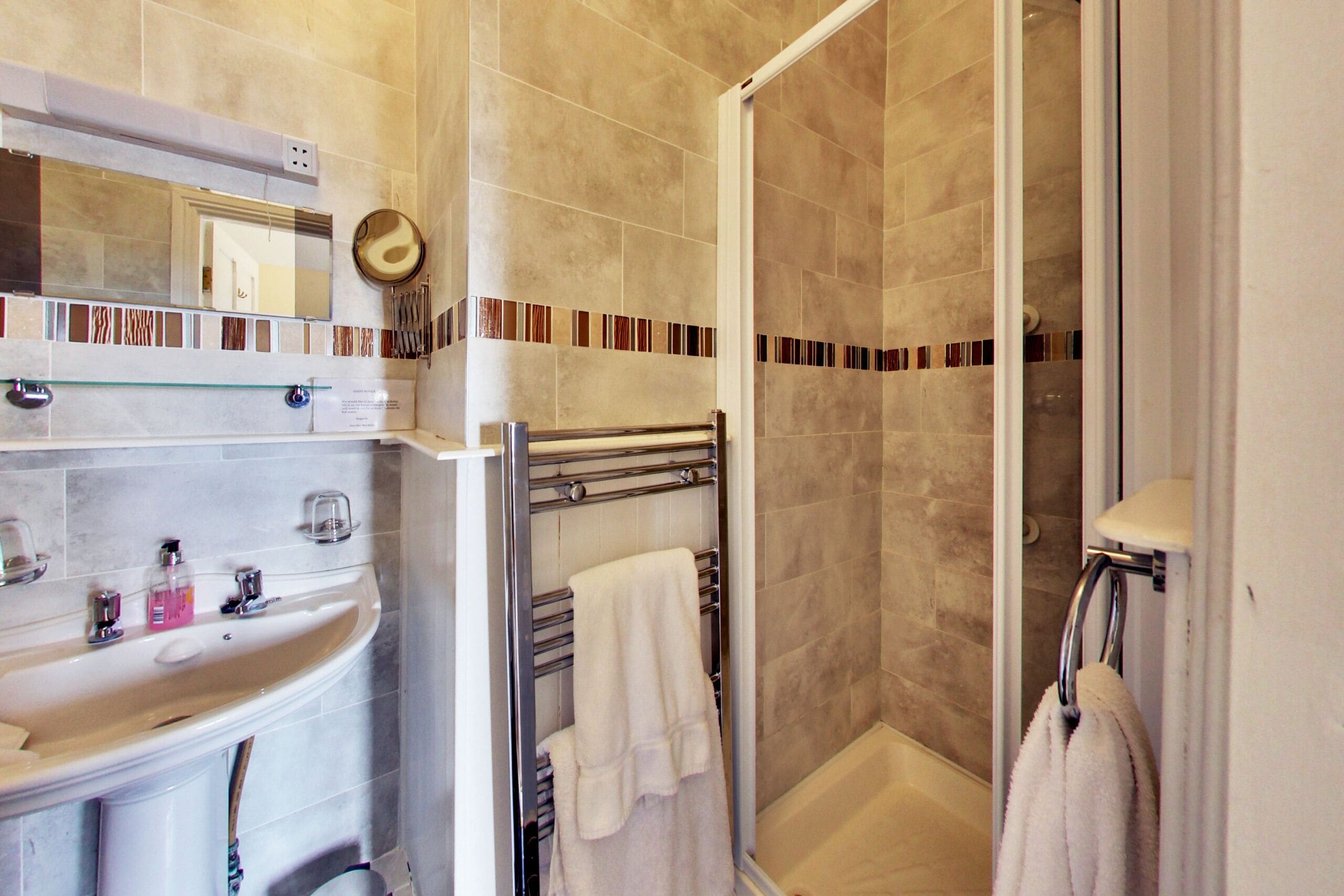 A bathroom with a sink, mirror, towel rack, and shower area.
