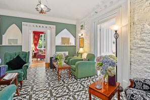 Una habitación con sofás tapizados en verde, suelo estampado y pared de ladrillo blanco.