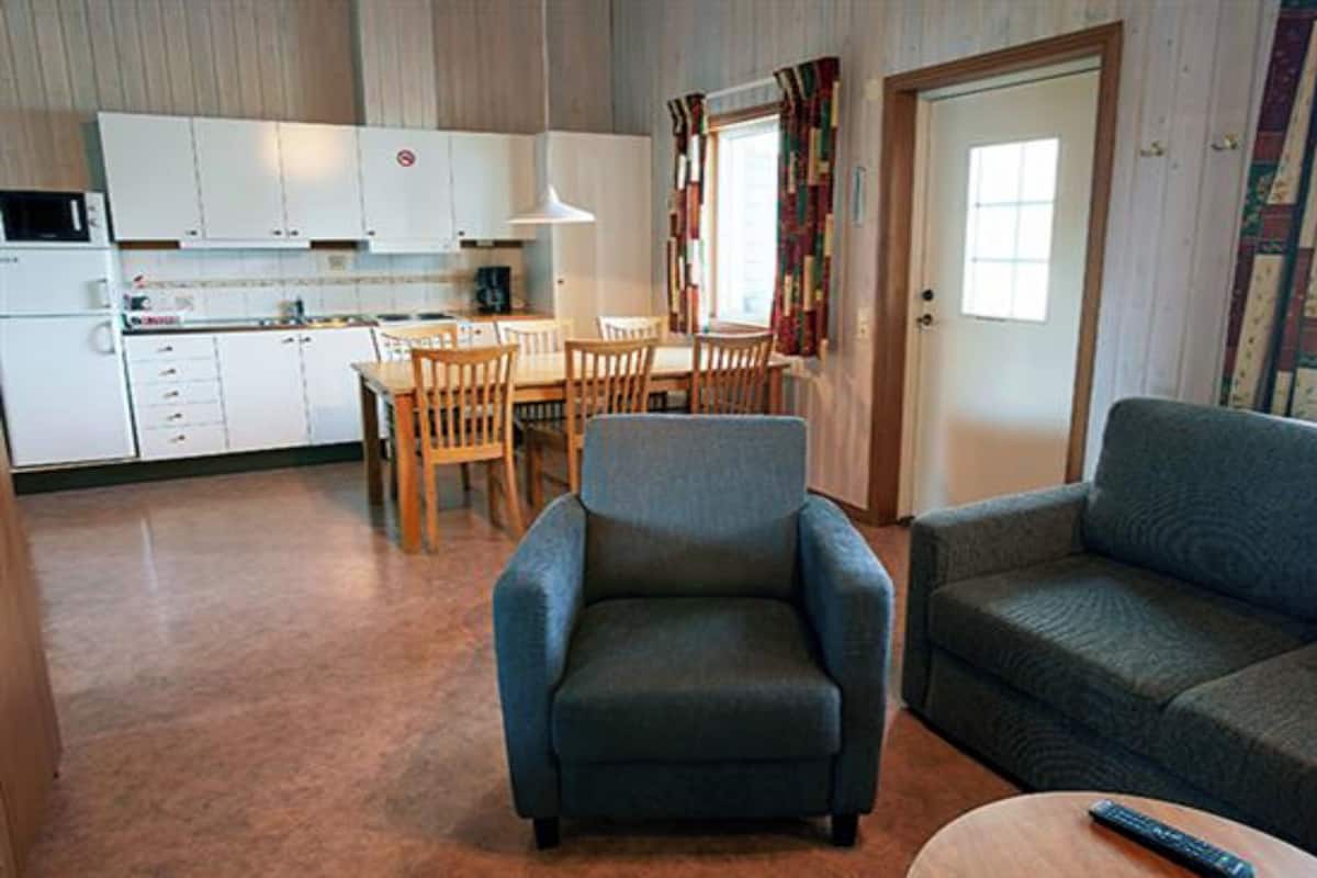 Un espace de vie compact comprenant un coin cuisine, un coin repas et un coin salon avec un canapé et un fauteuil.