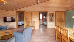 L’intérieur d’une cabane en rondins, avec un téléviseur, un coin salon et une table à manger.