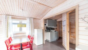 Une cabane en bois comprenant un coin cuisine, une table à manger avec des chaises et un réfrigérateur.
