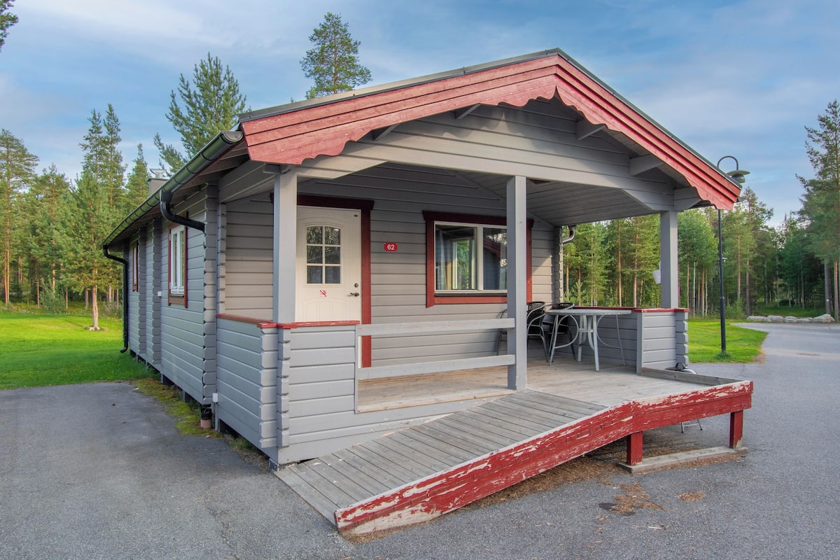 Une petite cabane avec un porche, une porte marquée du numéro « 62 » et une rampe d’accès pour fauteuils roulants.