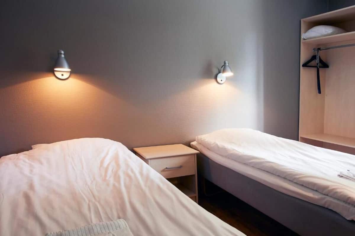 Une chambre avec deux lits simples, une table de chevet, une armoire et deux lampes fixées au mur.