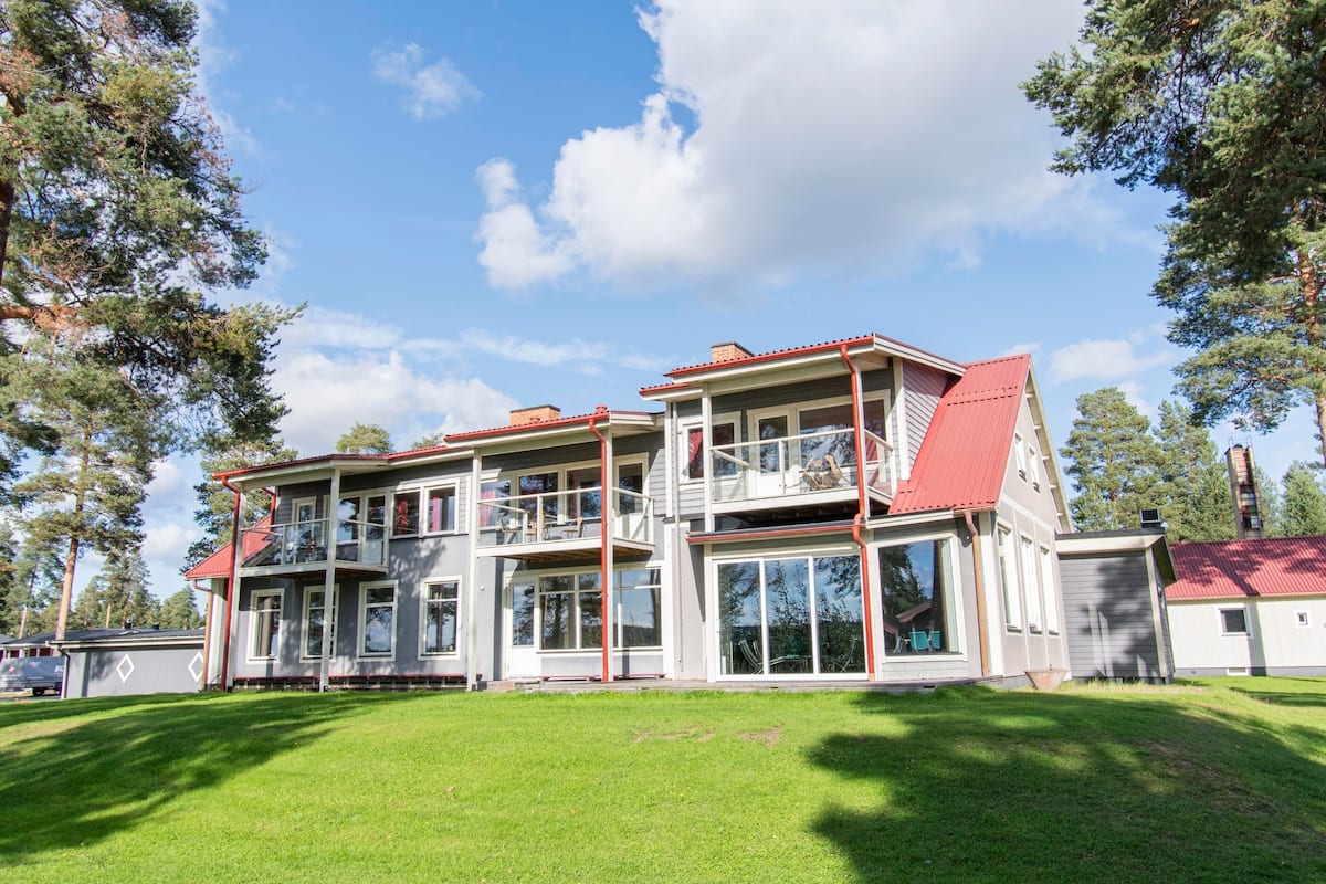 Une maison à deux étages avec un toit rouge, de grandes fenêtres et un balcon.