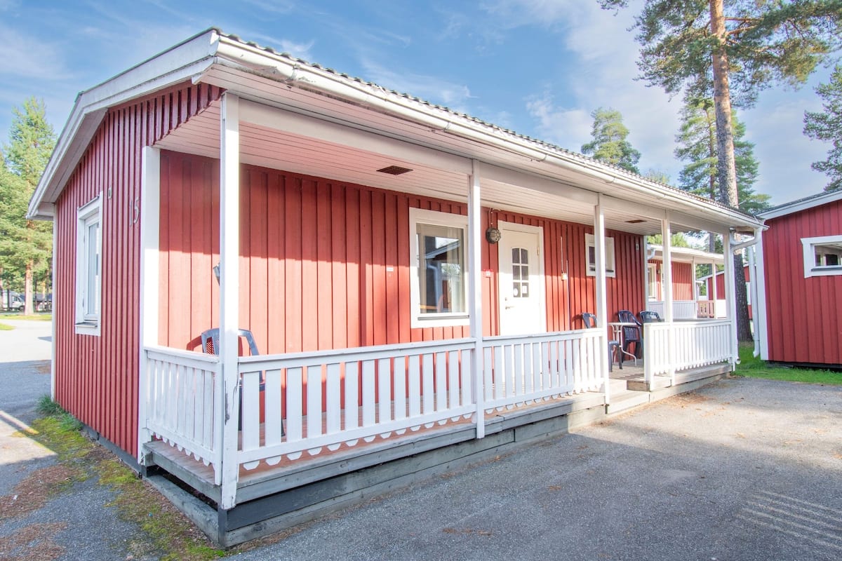 Une cabane en bois rouge, dotée d’un porche blanc et d’une petite dépendance attenante.