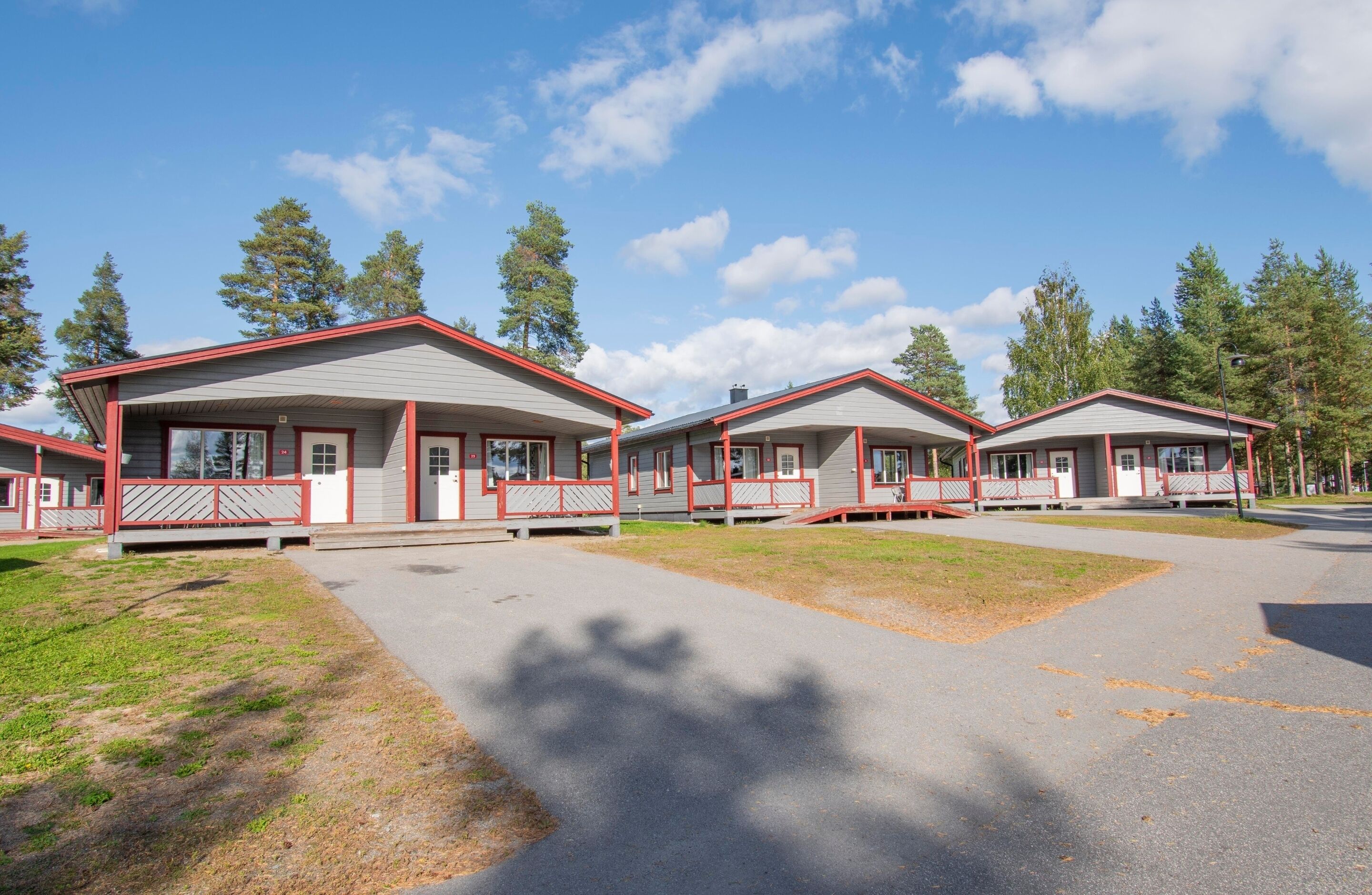A row of cabins with red trim, a paved driveway, and surrounding trees.