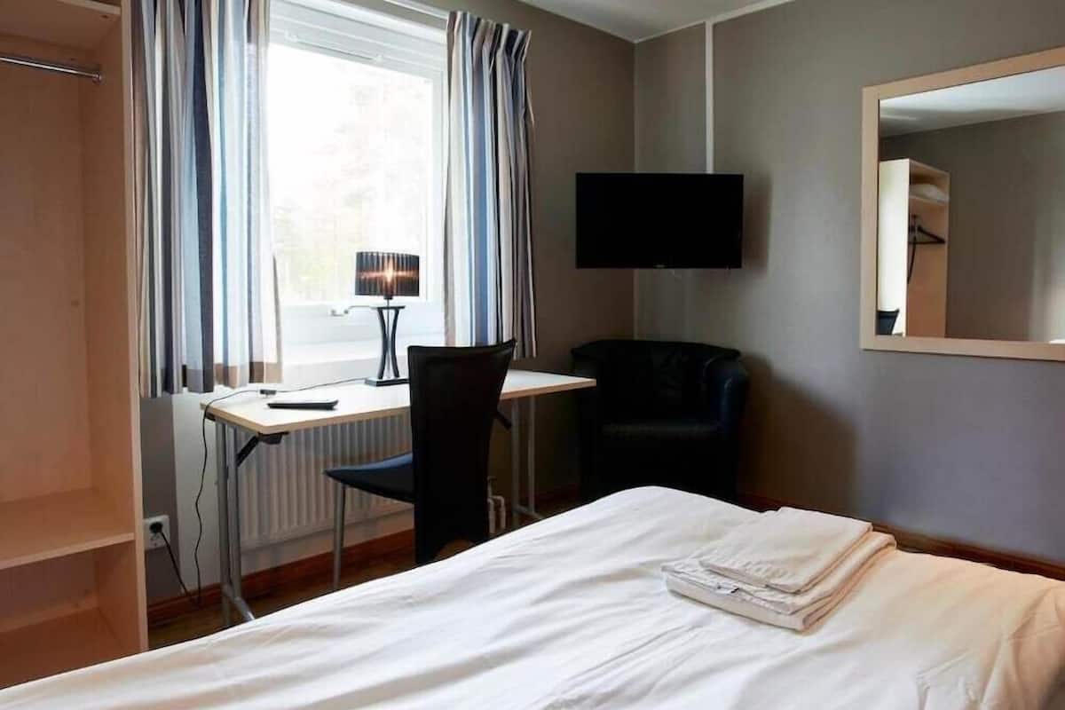 Une chambre d’hôtel avec un lit, un bureau, une chaise, une télévision et une fenêtre avec des rideaux.