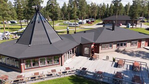 Un chalet doté d’un toit conique remarquable, d’une terrasse couverte avec des sièges d’extérieur et offrant une vue sur la forêt environnante.
