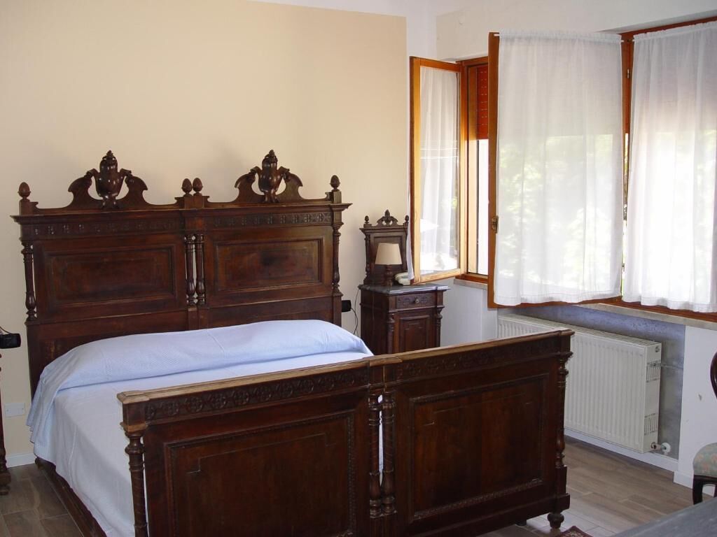 Ein Schlafzimmer mit einem großen Holzbett, einem kleinen Nachttisch und einem Fenster mit Vorhängen.