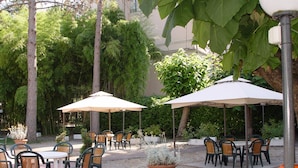 An outdoor patio with tables and chairs, surrounded by greenery and covered by umbrellas. - Hotel Villa delle Fonti (Riolo Terme)