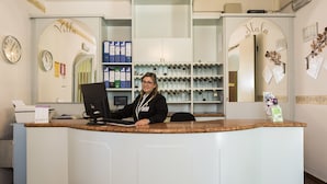 A reception desk with a computer, a clock, and a counter with a nameplate. - Hotel Villa delle Fonti (Riolo Terme)