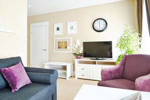 A living room with a sofa, armchair, TV, white entertainment unit, and a clock on the wall. - Old Street Kostroma (Kostroma)