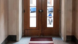 A hallway with a red carpet leading to a double wooden door with glass panels. - Camere del Cavaliere (Rome)