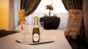 A bottle of Maschio Prosecco on a table with two glasses, set in a room with a bed, a chair, and a window with curtains. - Camere del Cavaliere (Rome)