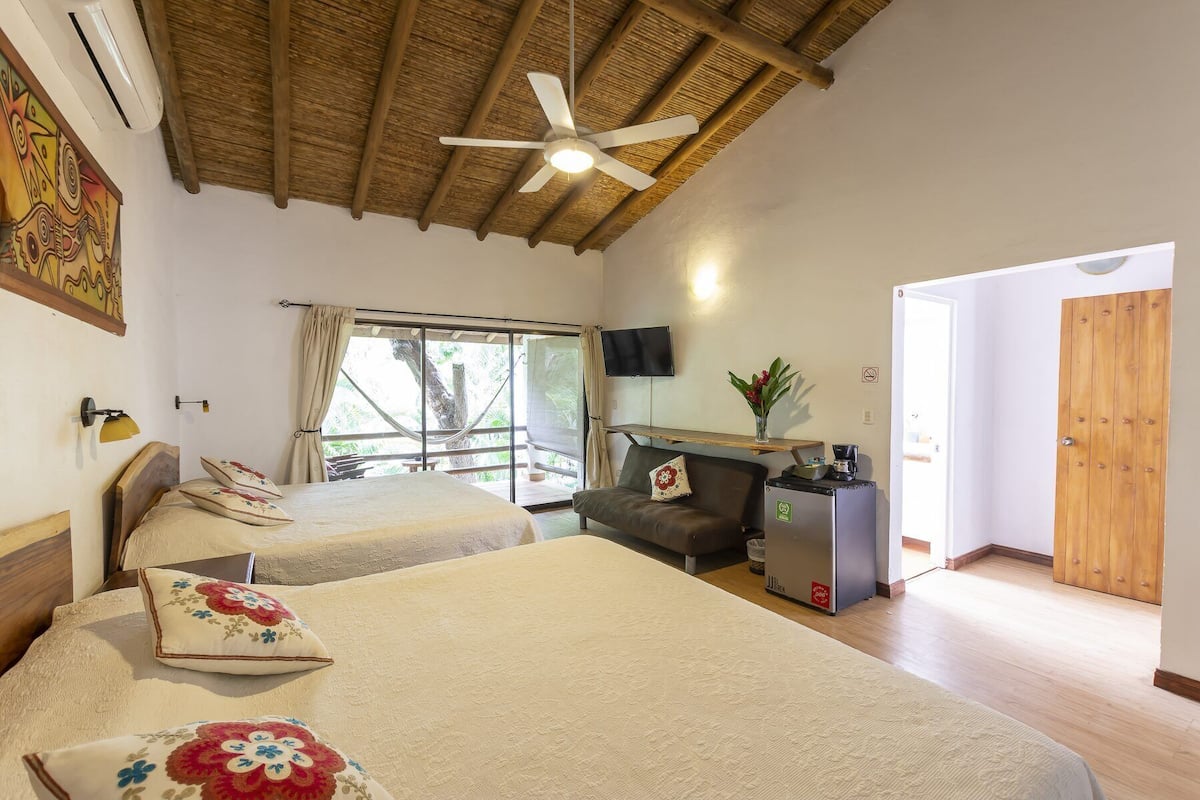 A bedroom with two beds, a ceiling fan, a TV, a coffee machine, and a view of the outdoors.