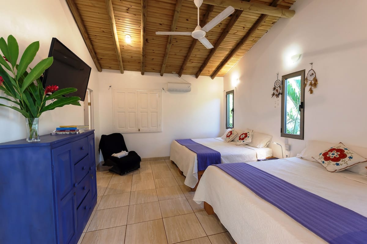 A room with two beds, a blue dresser, a ceiling fan, and a TV mounted on the wall.