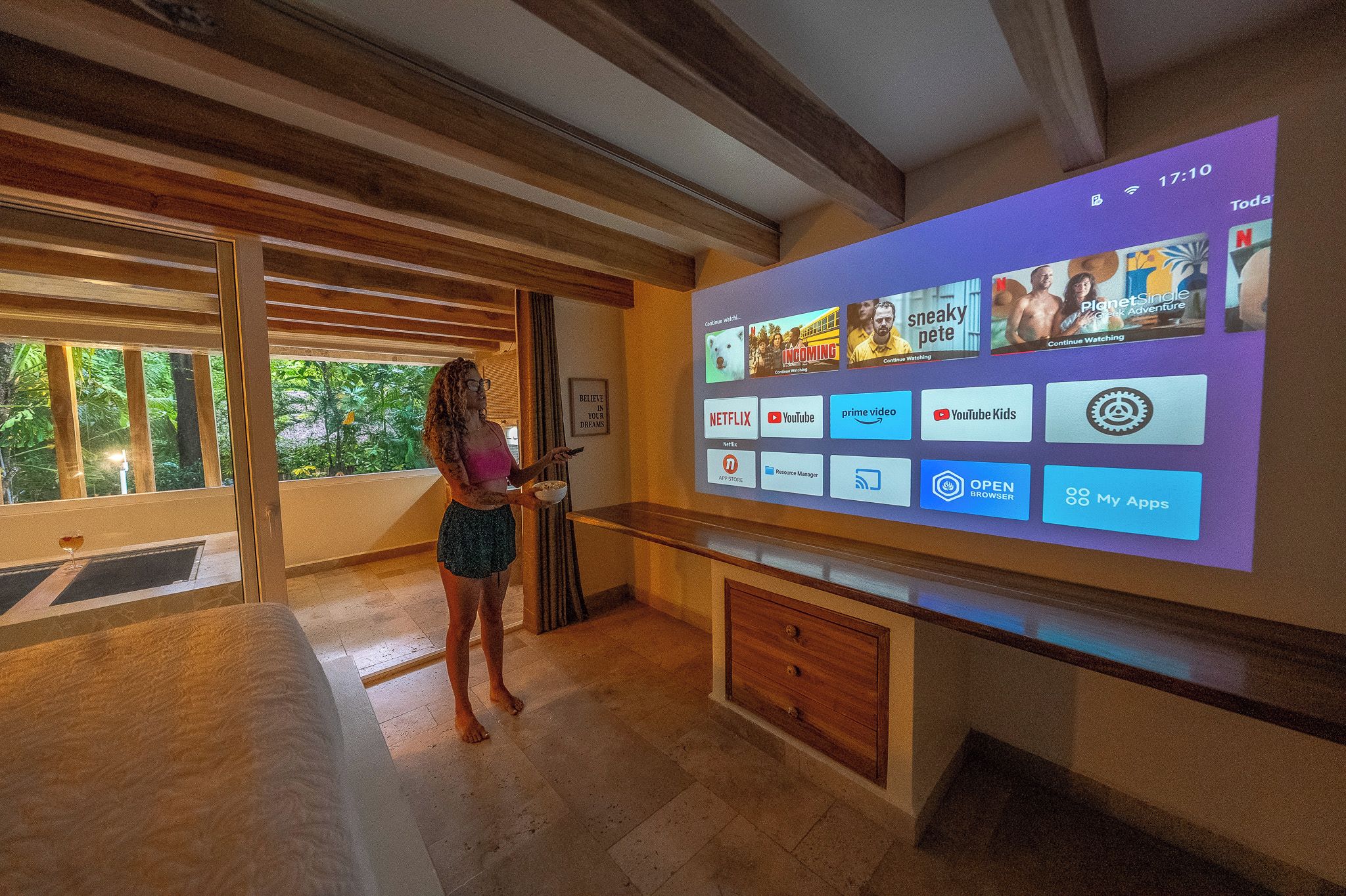 A woman standing in a room with a large screen displaying various streaming services.