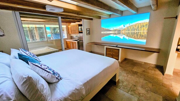 A bedroom with a bed, a TV, a window, and a view of a lake. - Atrapasuenos Dreamcatcher Hotel (Cóbano)
