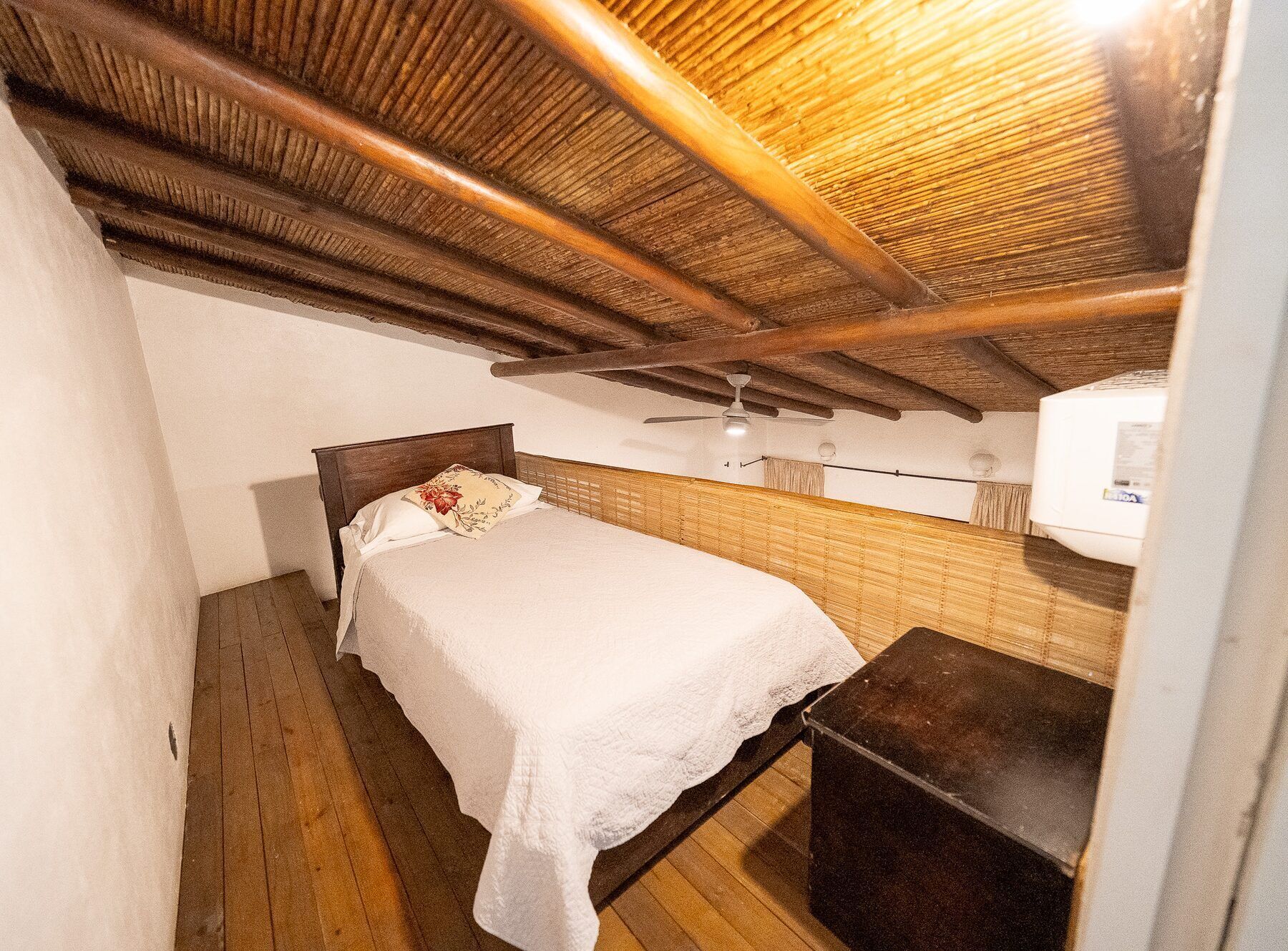 A small, single-bed room with a wooden ceiling and a ceiling fan.