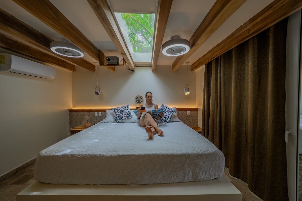 A bedroom with a large bed, a skylight, and a ceiling fan.