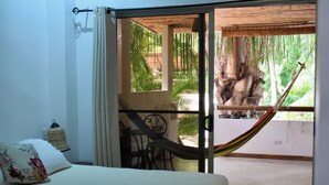 A room with a bed, a hammock, and a view of a garden with palm trees. - Atrapasuenos Dreamcatcher Hotel (Cóbano)
