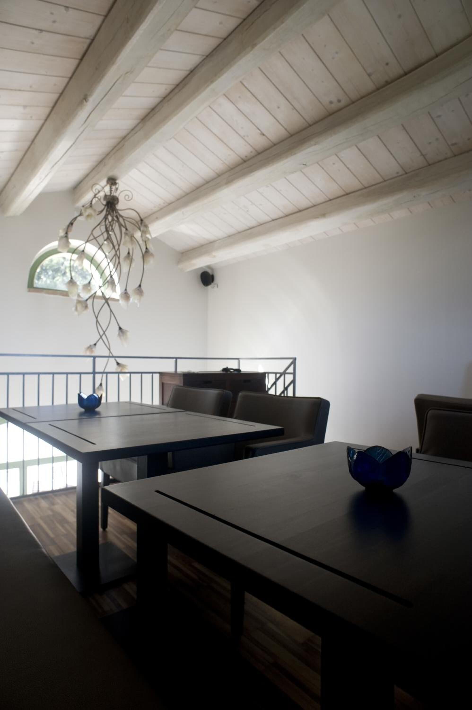 A dining area with a high ceiling and exposed beams, a chandelier, and a view of the outdoors.