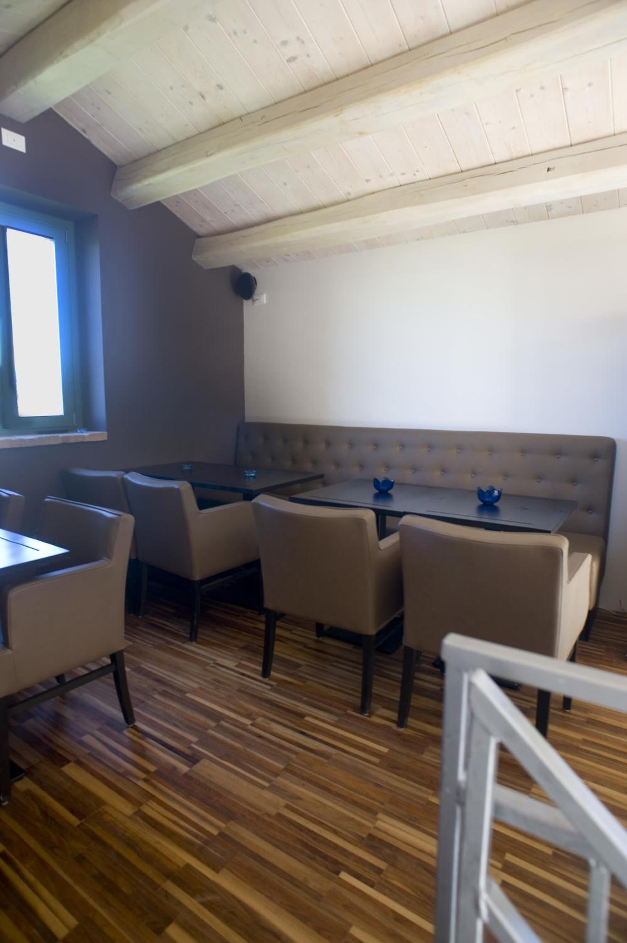 A dining area with a wooden ceiling, a window with blinds, a cushioned bench, and a table with chairs.