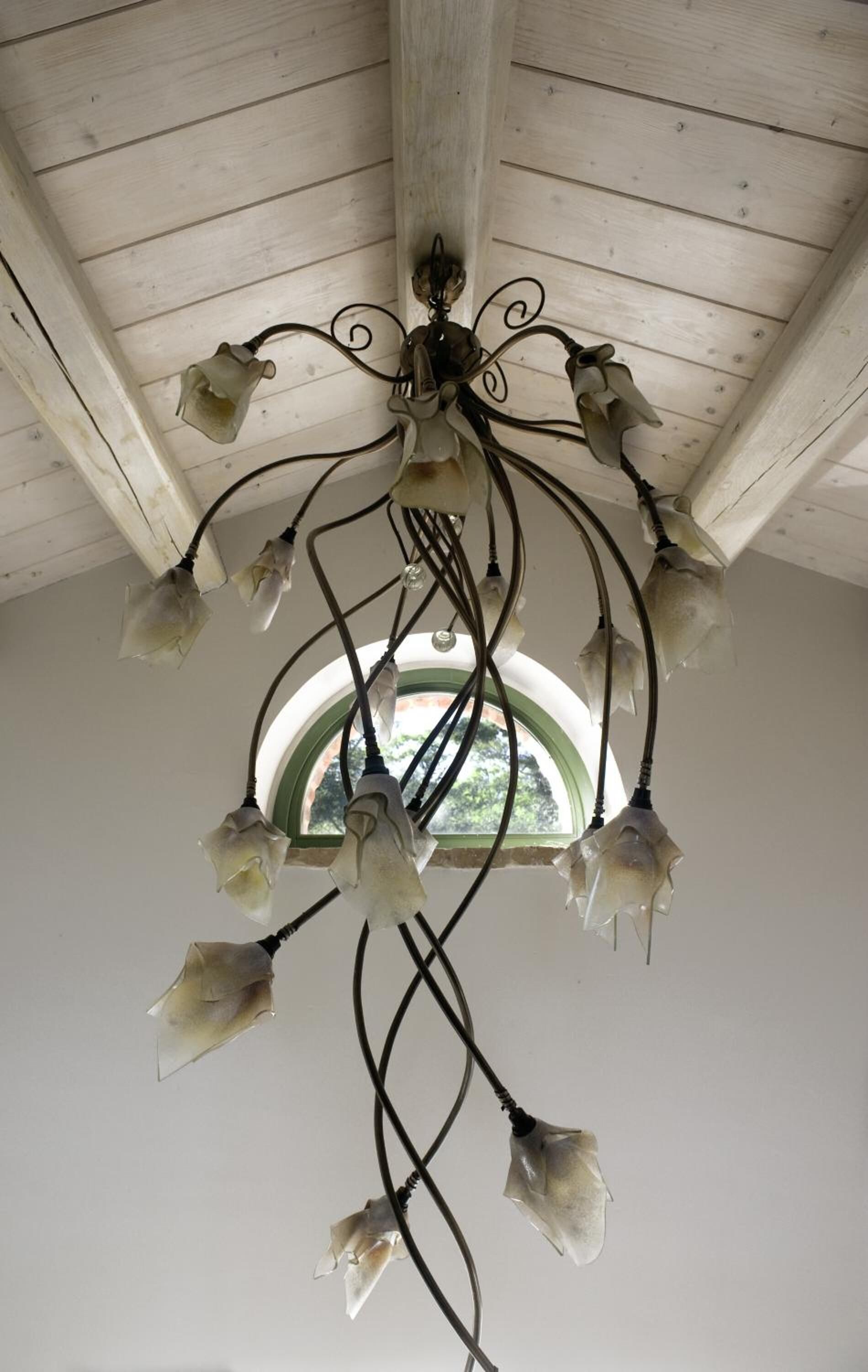 A chandelier with multiple light fixtures hanging from a wooden ceiling with a circular window.
