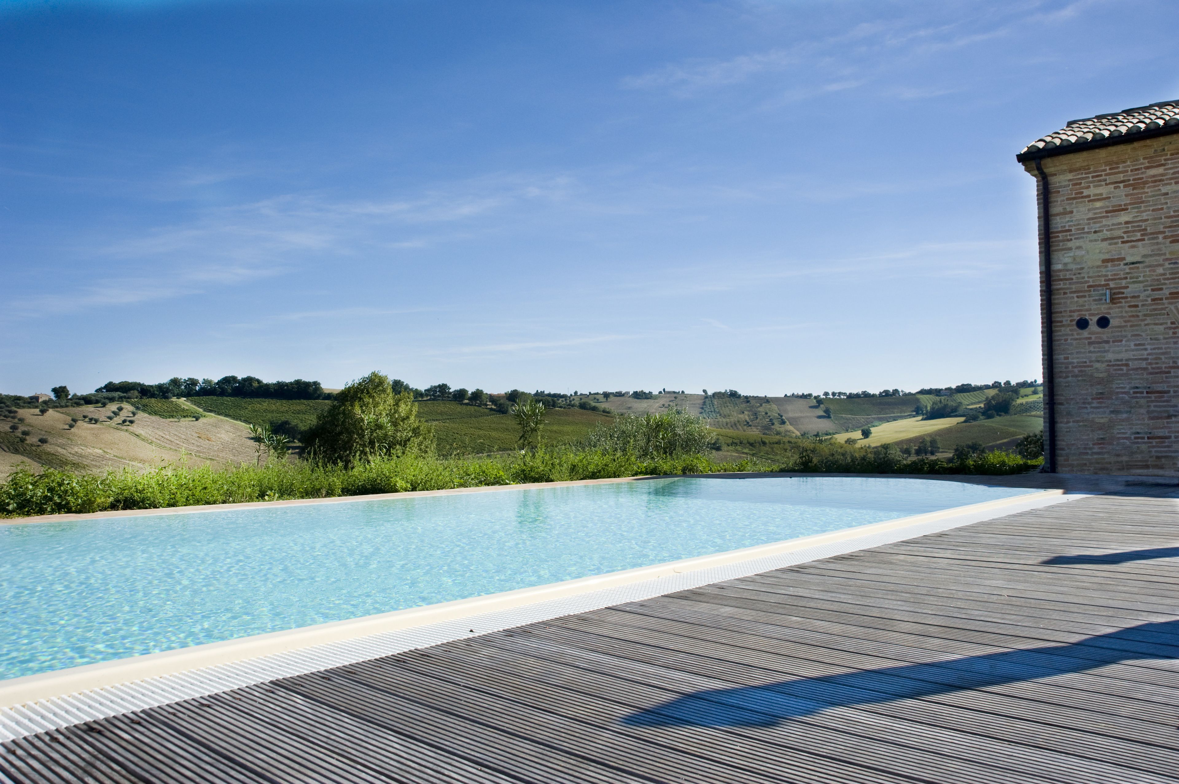 Une piscine avec une terrasse en bois et, en arrière-plan, une vue sur des collines ondoyantes.