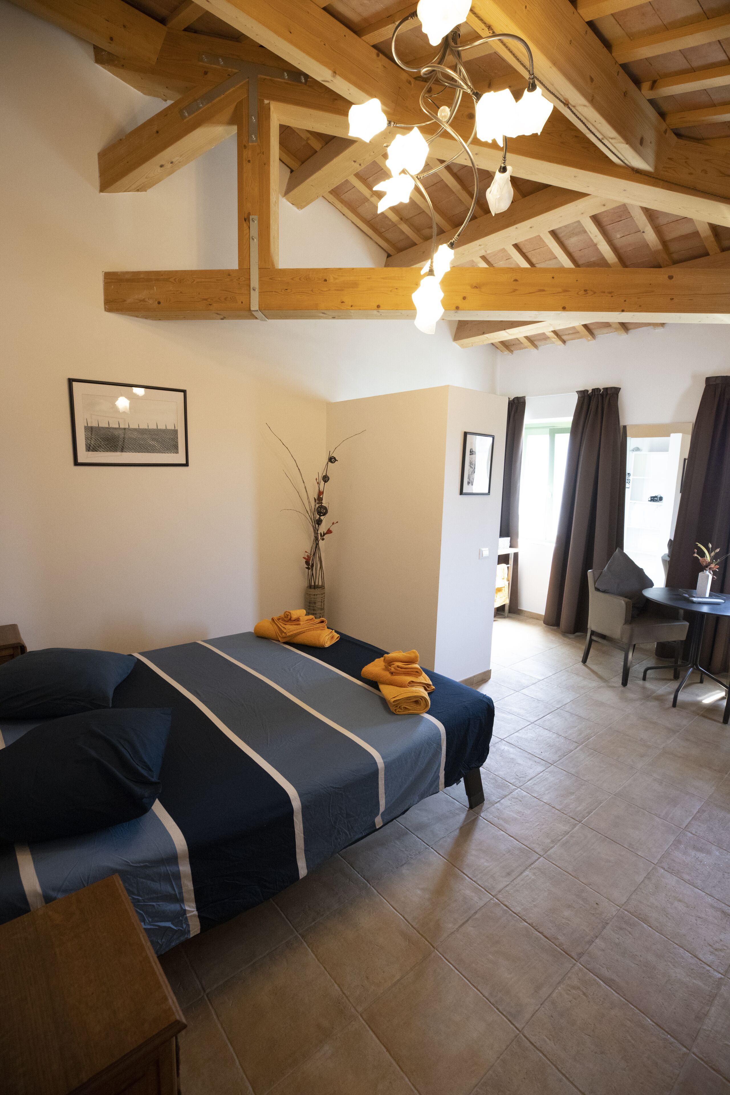 Une chambre à coucher comprenant un lit, un bureau, une chaise, un vase avec des plantes et un luminaire au plafond.
