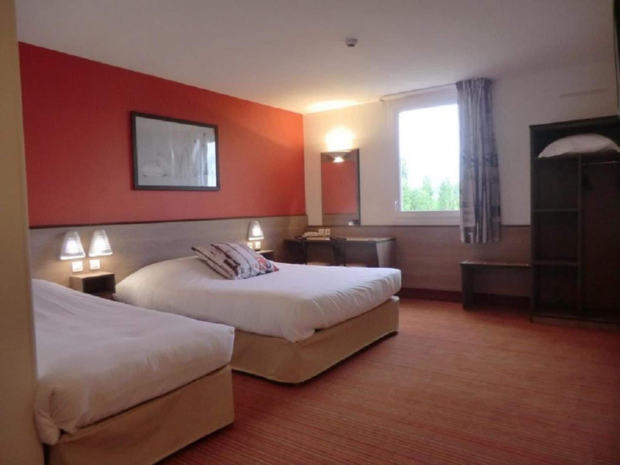 A hotel room with two beds, a desk, a chair, a window with curtains, a mirror, and a wall-mounted picture.