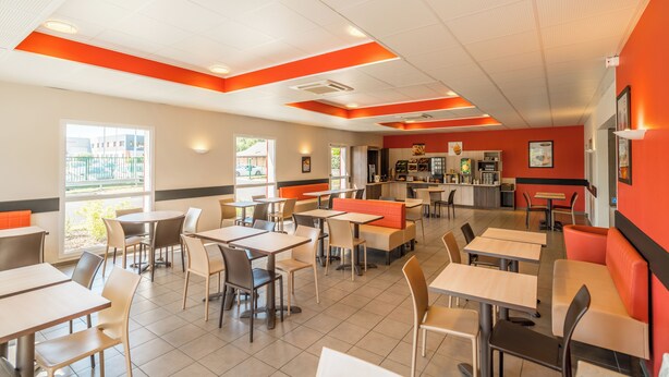Een restaurant met meerdere tafels en hoekjes, een balie en uitzicht op buiten.