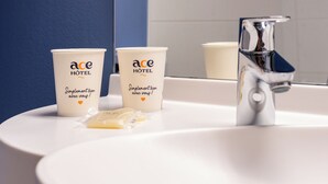 Twee witte bekers met de branding 'ace HOTEL' en een zilveren kraan op een witte wasbak.