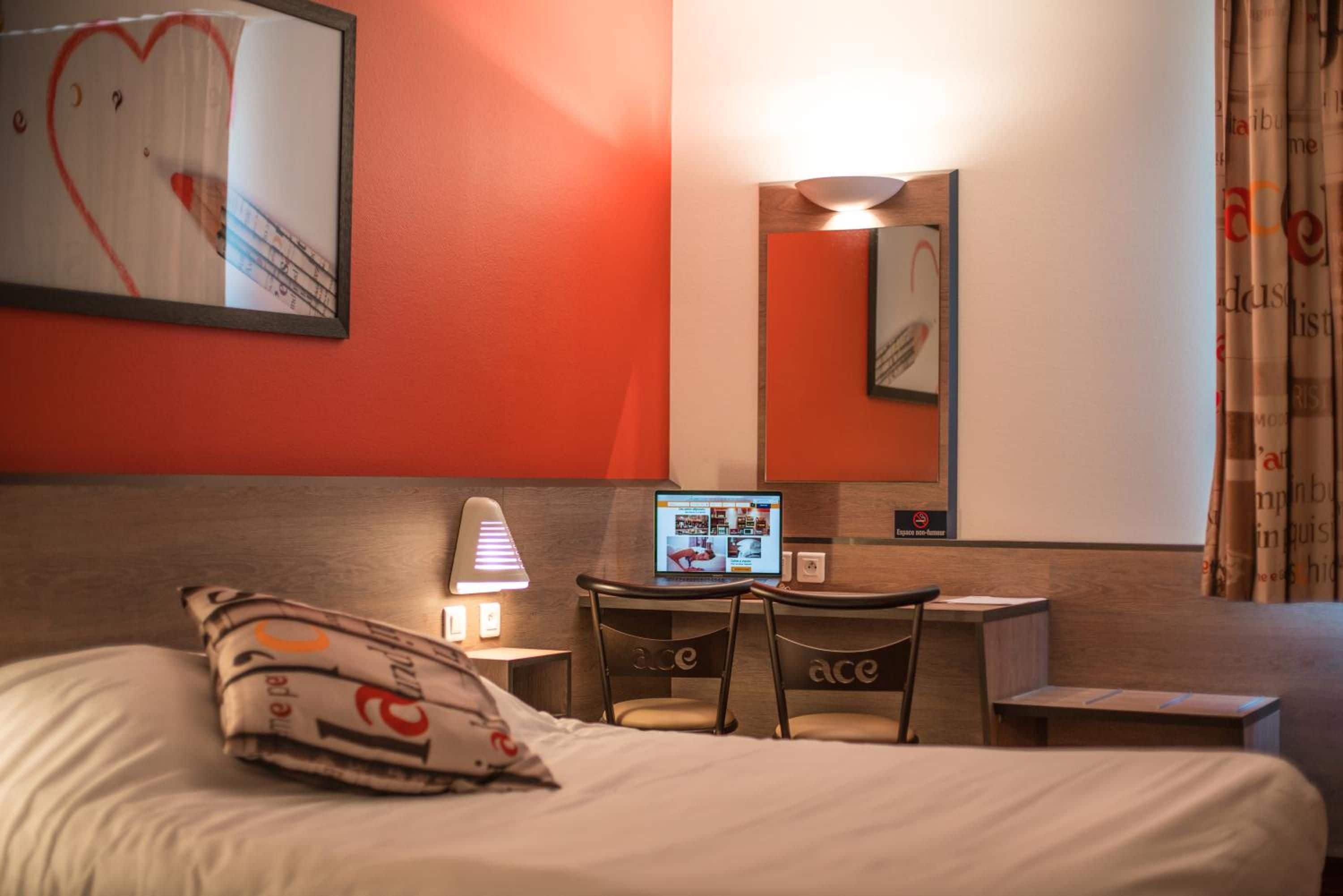 Habitación de hotel con cama, escritorio con una computadora portátil, una silla, una lámpara y un cuadro con forma de corazón en la pared.