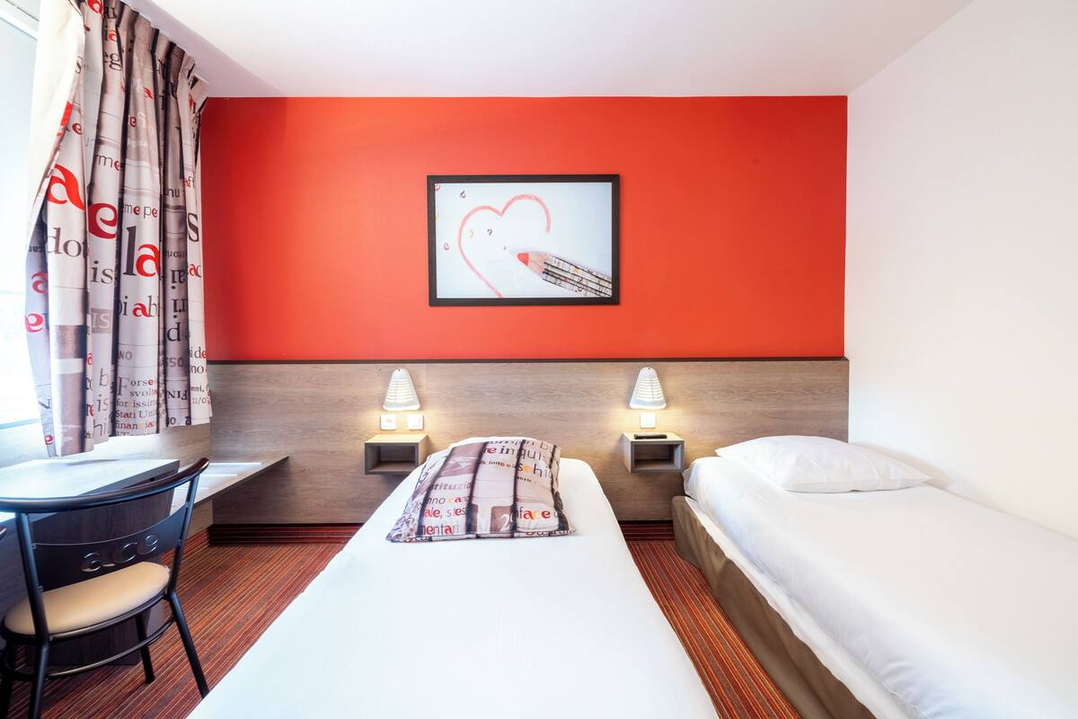 Une chambre d’hôtel avec un lit, un bureau, une chaise, deux lampes de chevet et un tableau encadré au mur.