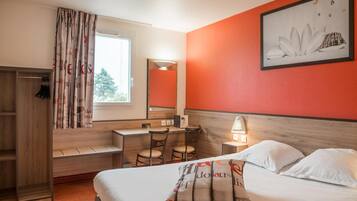 Ein Hotelzimmer mit Bett, Schreibtisch, Stuhl, Kleiderschrank und einem fenster mit Vorhängen.