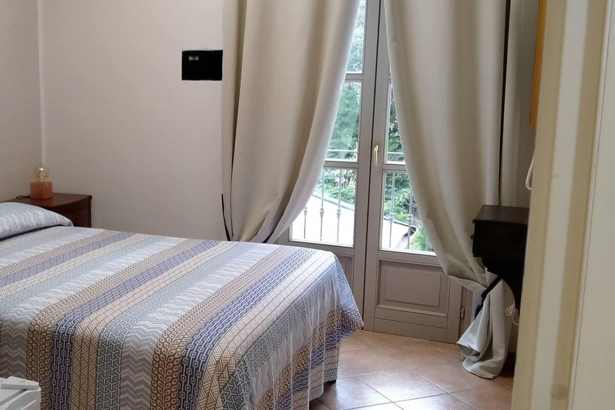 A bedroom with a bed, a bedside table, a lamp, and a window with curtains.