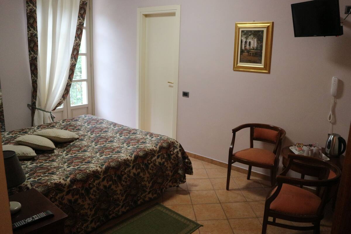 A bedroom with a bed, a chair, a desk, a telephone, and a picture on the wall.