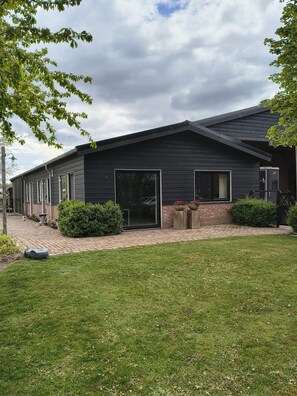 A modern house with a dark exterior, large glass doors, and a paved driveway. - Studio Verhuur Jamzes (Hoogerheide)