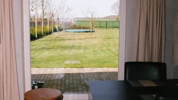 Een kamer met een groot raam, een tafel, een zwarte stoel en een klein voetenbankje.