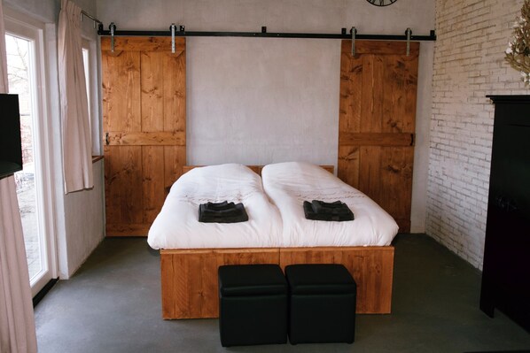A bedroom with a wooden bed frame, two pillows, and a bench. - Studio Verhuur Jamzes (Hoogerheide)