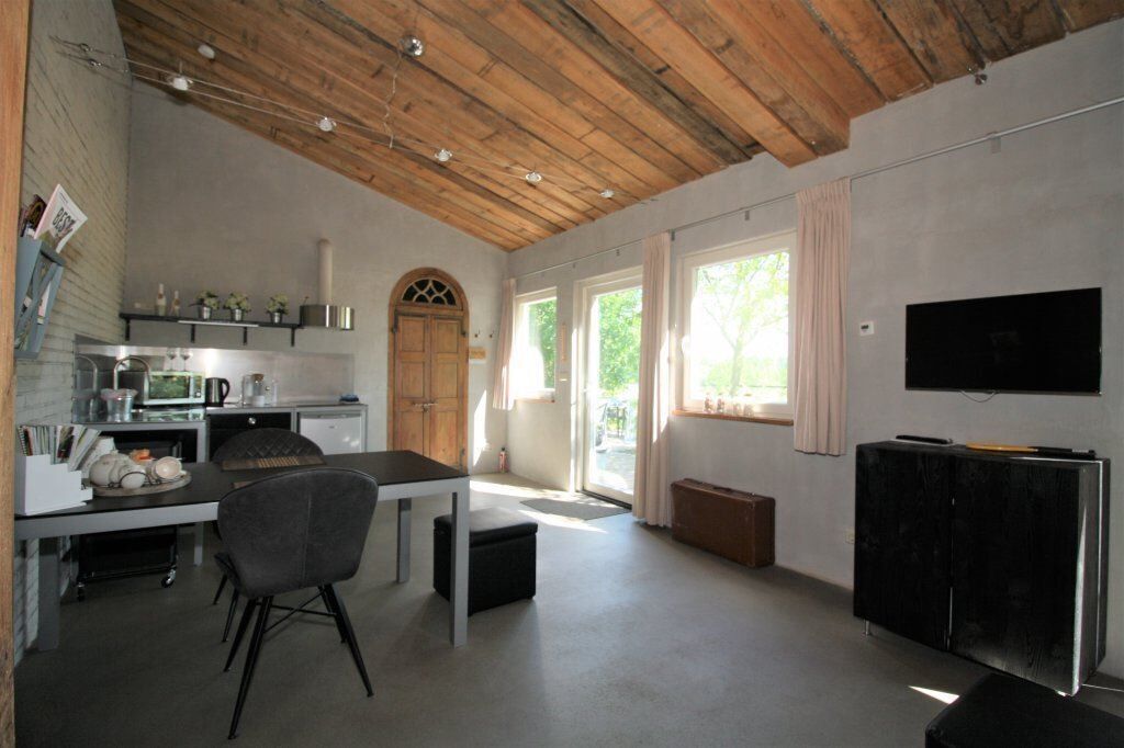A spacious kitchen with modern appliances, a dining area with a table and chairs, a large window with curtains, and a flat-screen TV mounted on the wall.